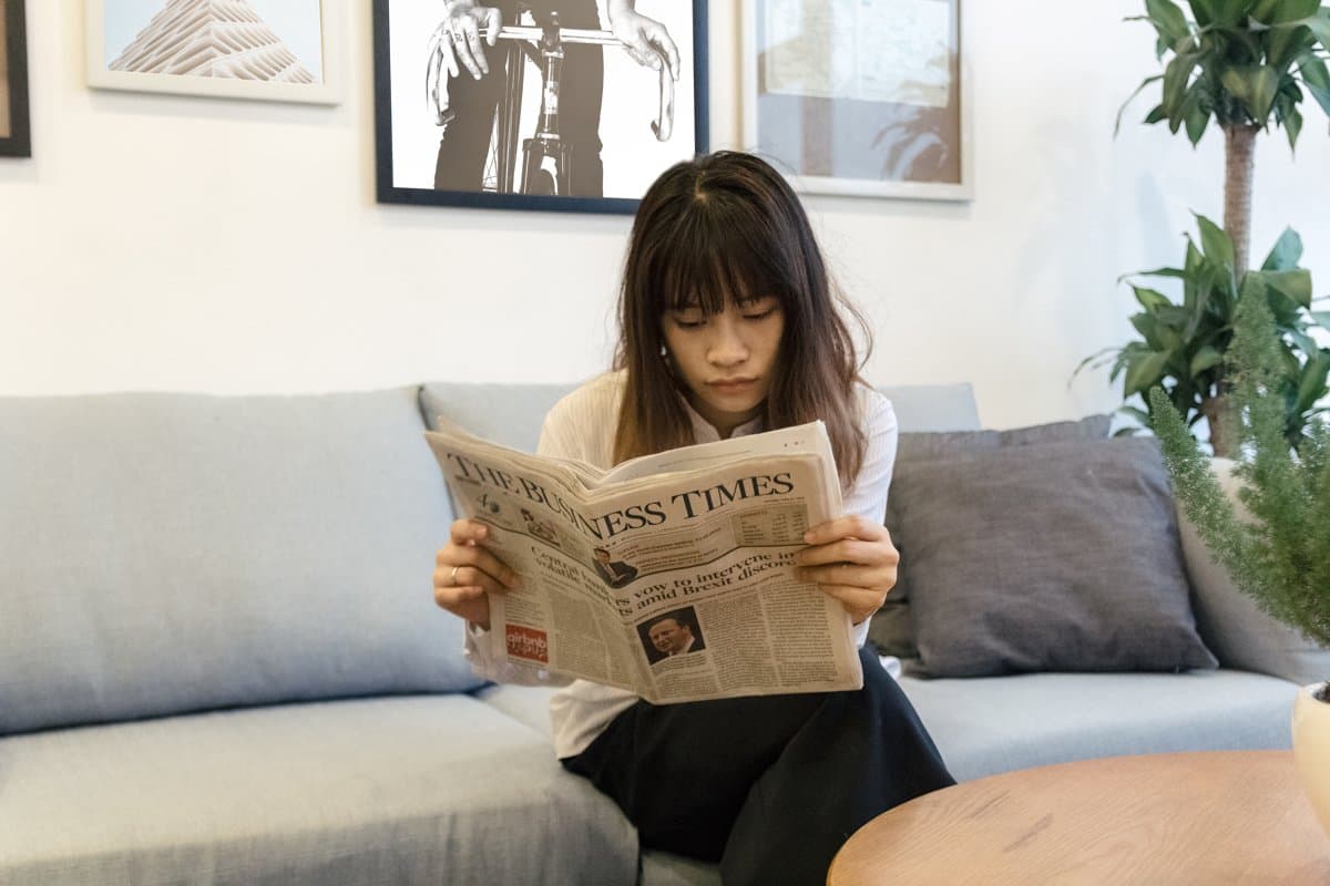 A reader on a sofa holding an open broadsheet newspaper