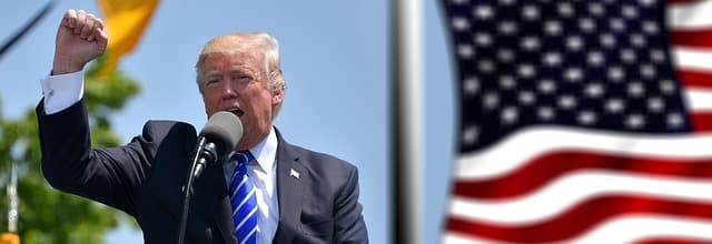 Donald Trump speaking at an outdoor podium beside an American flag